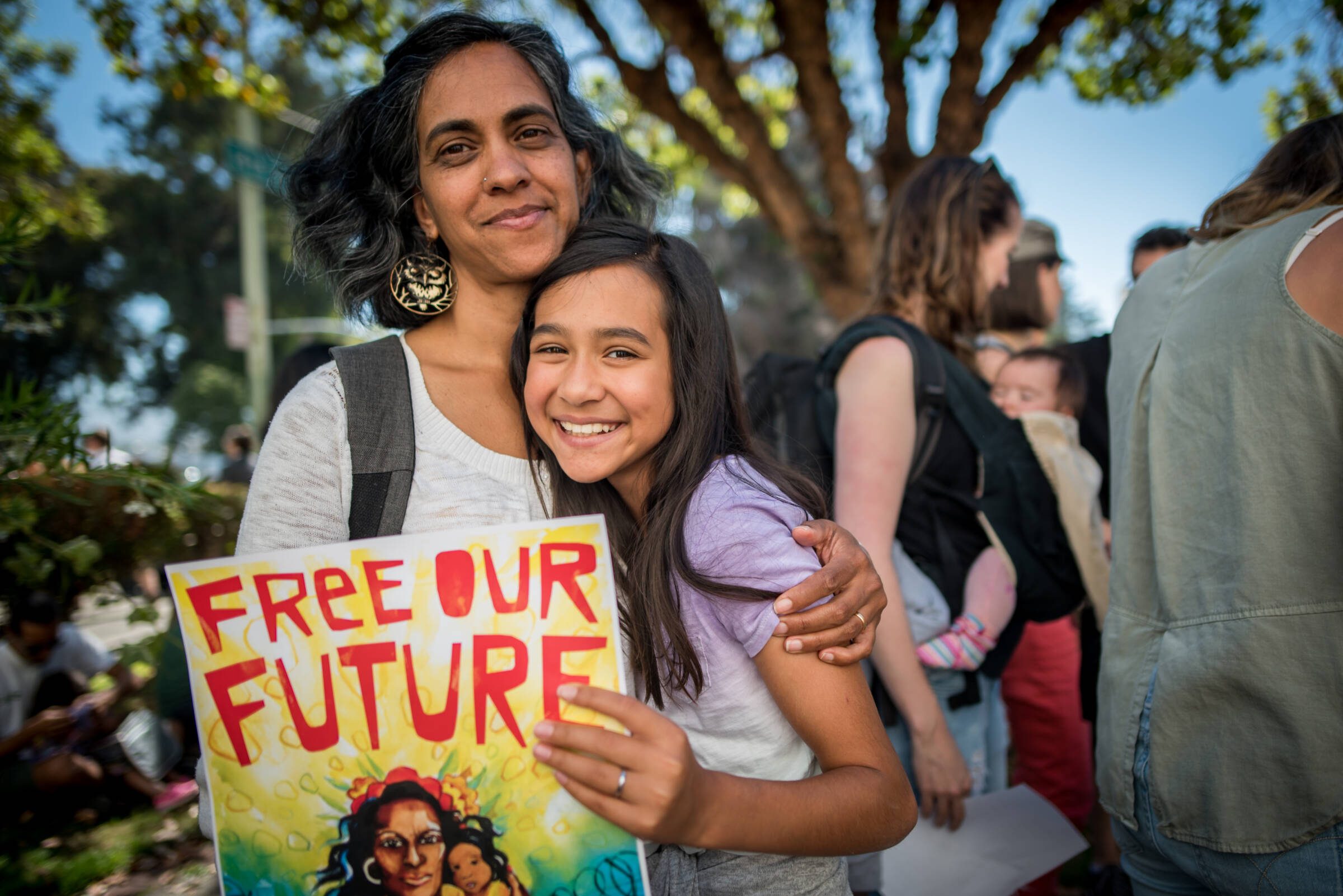 An adult embraces a teenager holding a sign that reads "Free Our Future"