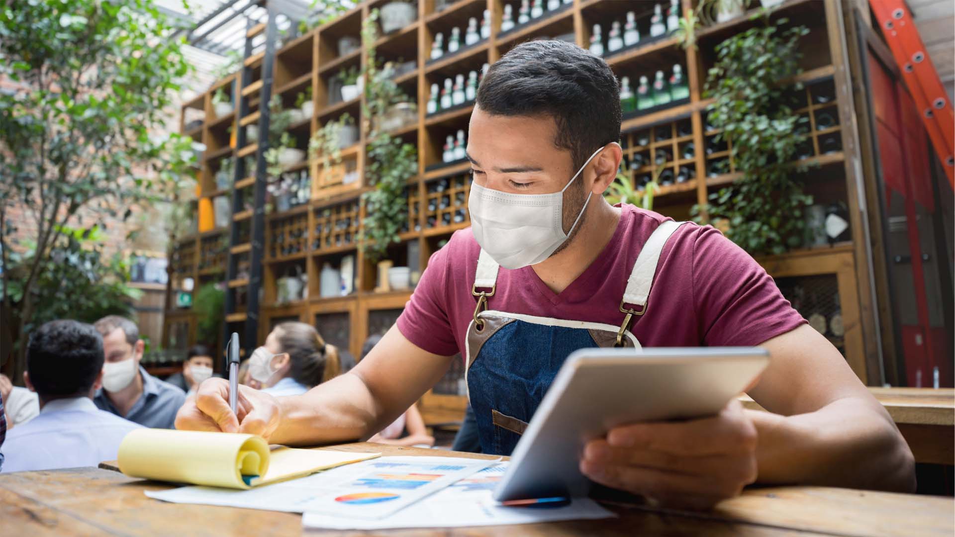 Man wearing a mask and writing on a notepad