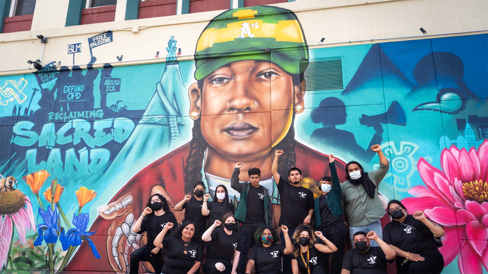 Group of people raising their fists, standing in front of a mural