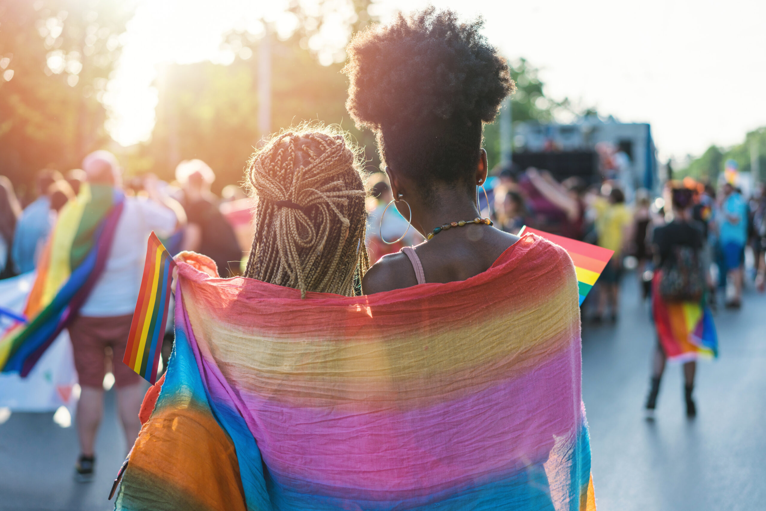 Two woman with a rainbow scarf wrapped around them