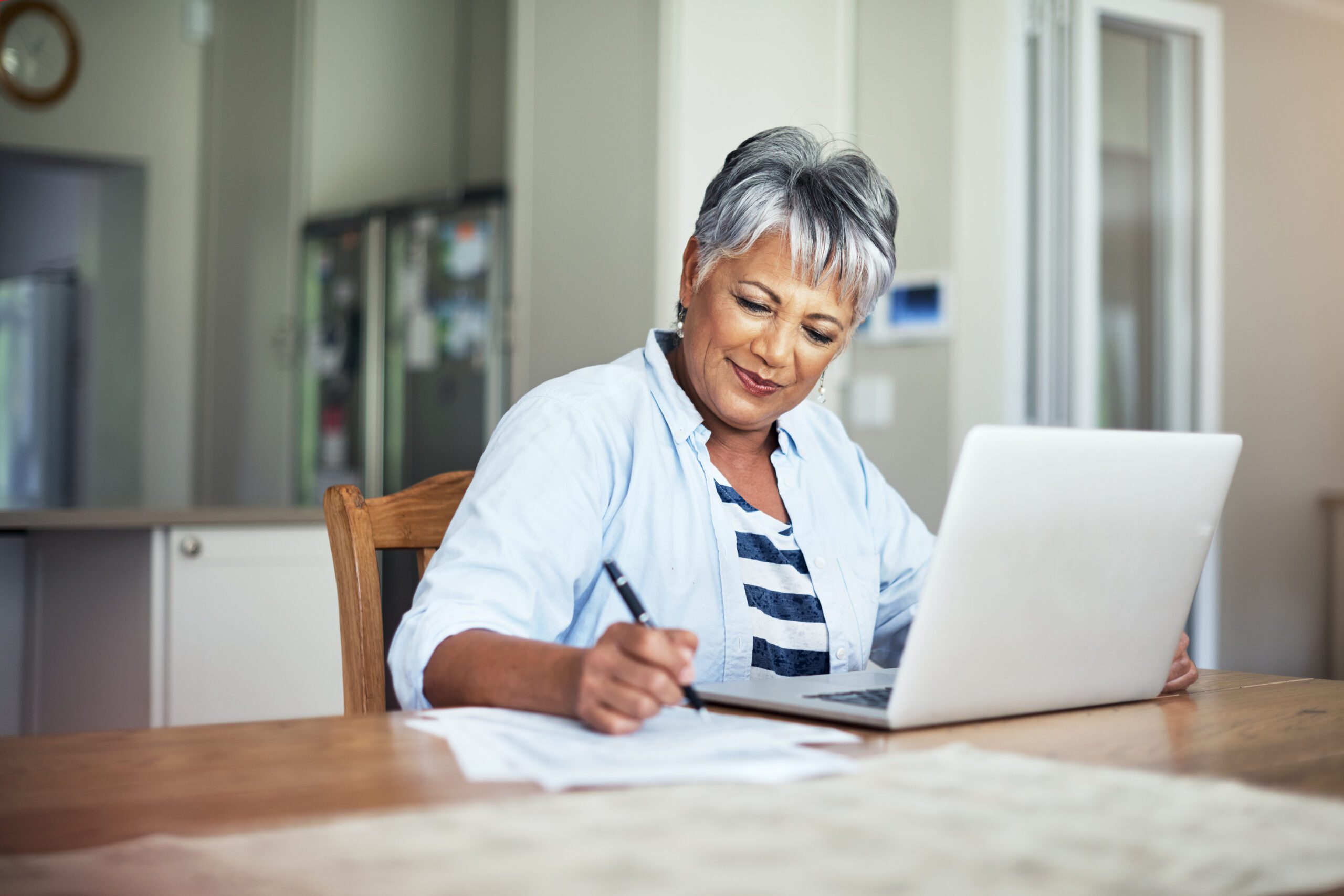 Cropped shot of a senior woman using a laptop and writing on a piece of paper.