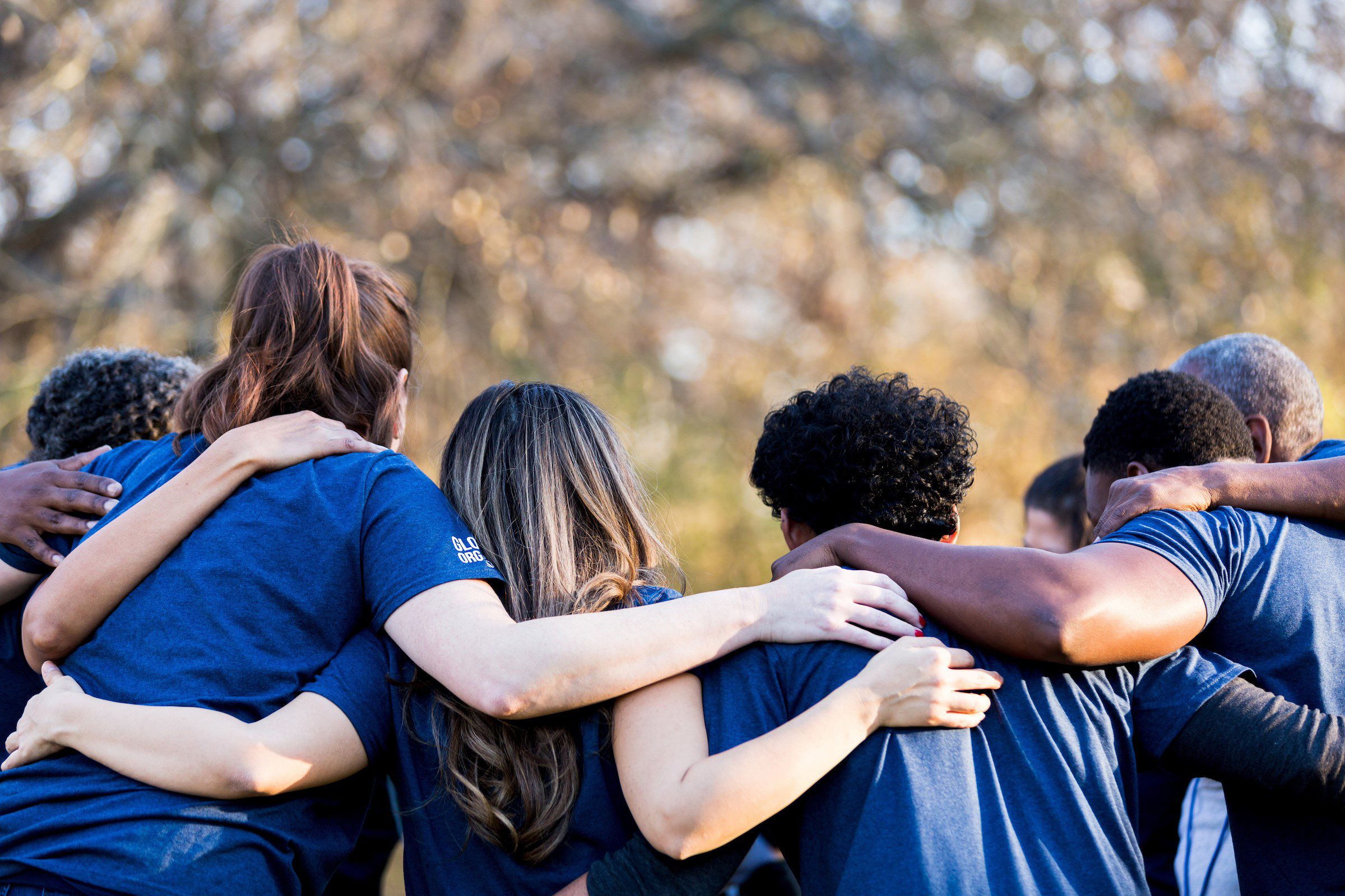 Diverse group of friends cleanup a park during a charity event. They are standing with their arms around one another.